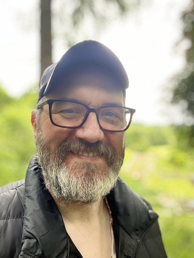Andy Sutton, smiling, in a cap and glasses outdoors