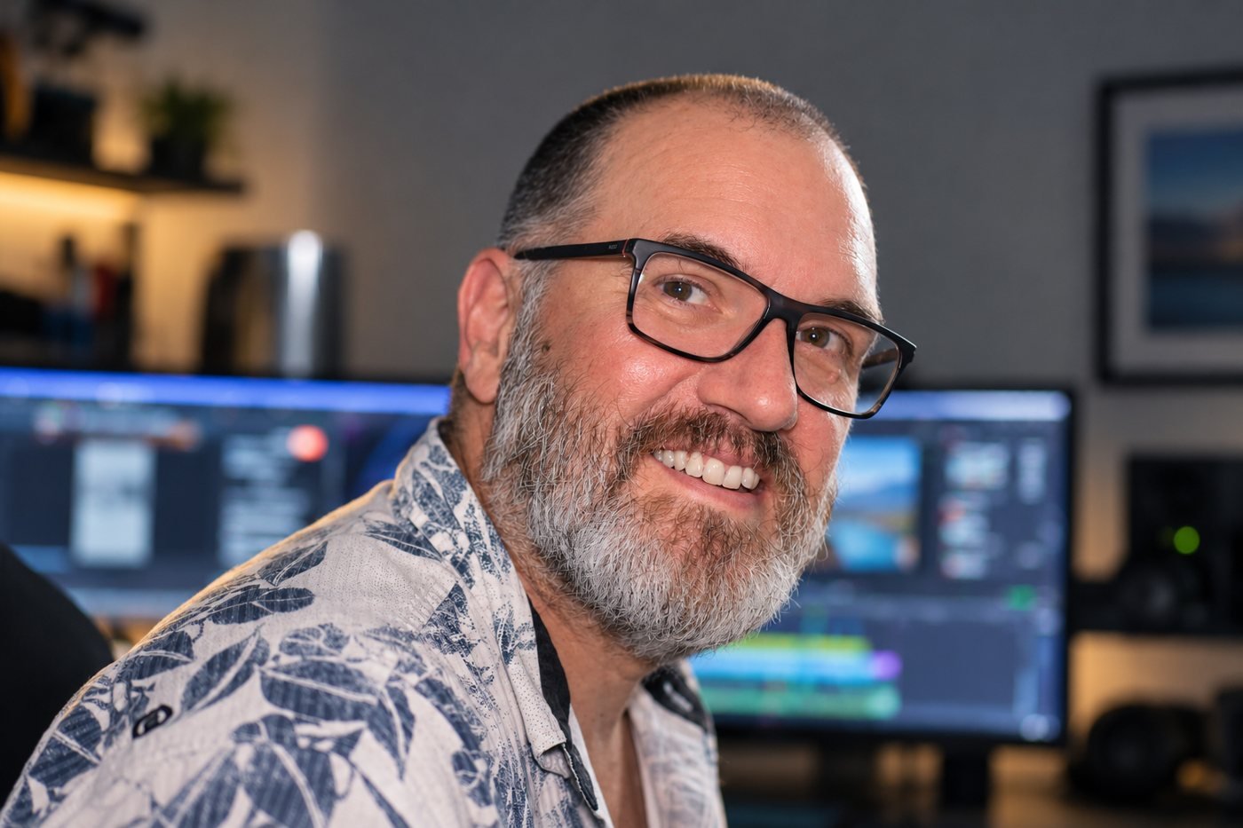 Andy Sutton smiling at his edit suite, a timeline on the screens behind him
