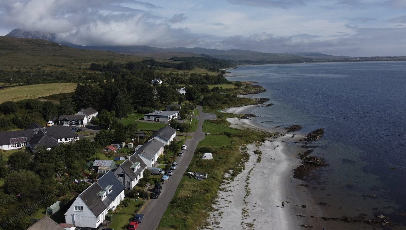 Drone shot of a white beach and a row of houses on the coast of Jura