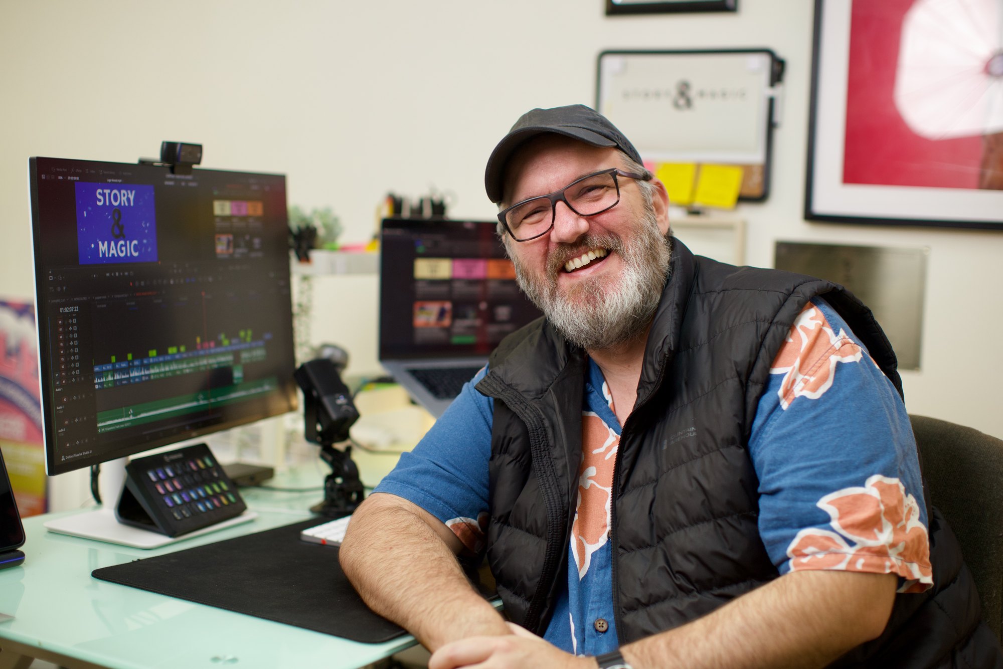Andy at his desk, smiling, with a Story and Magic edit open on the monitor beside him